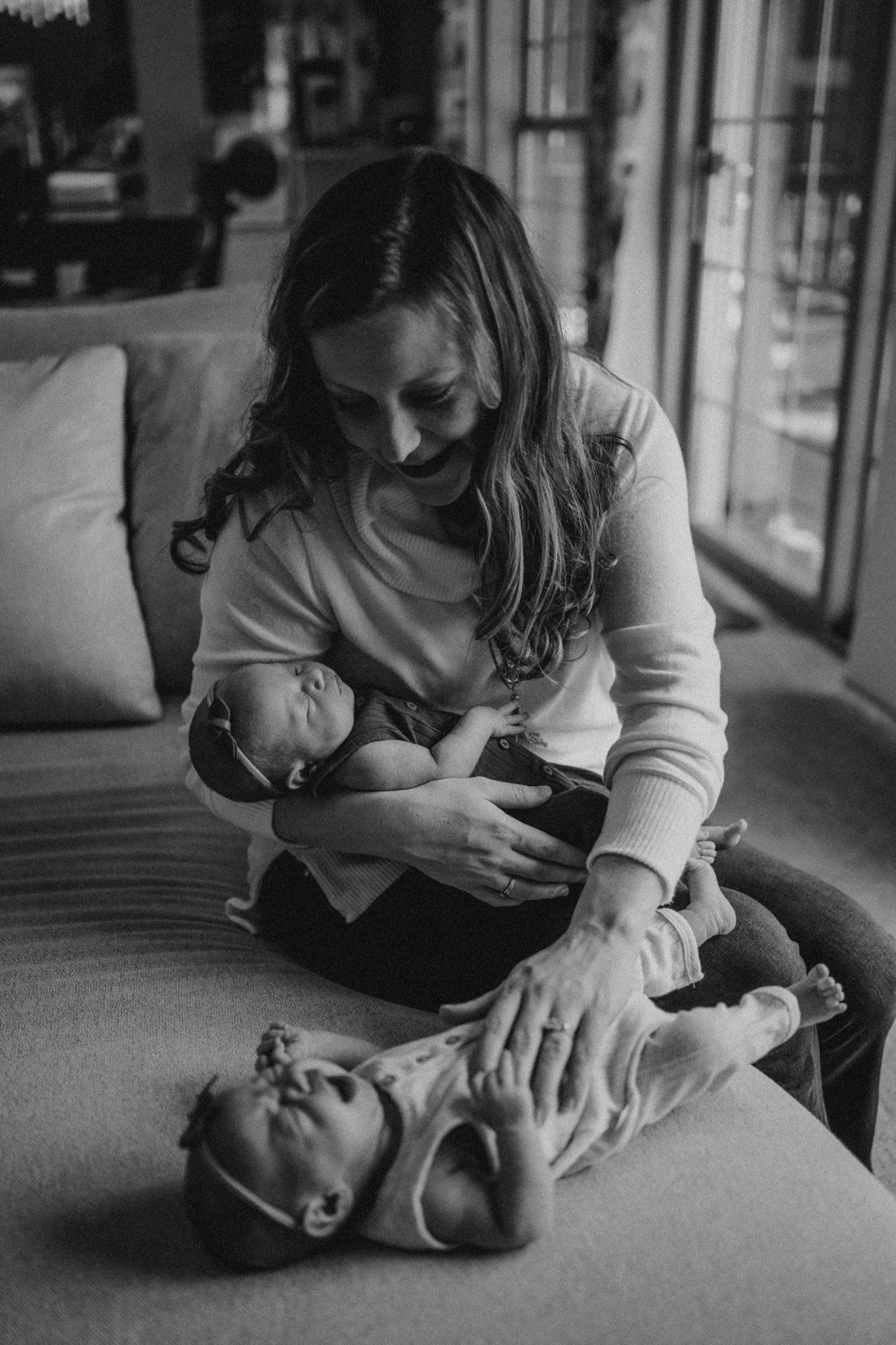 Black and white photo of mother tending to babies on living room couch.