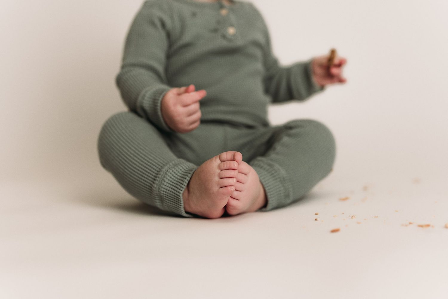 Overhead view of baby lying on cream background wearing green ribbed outfit.