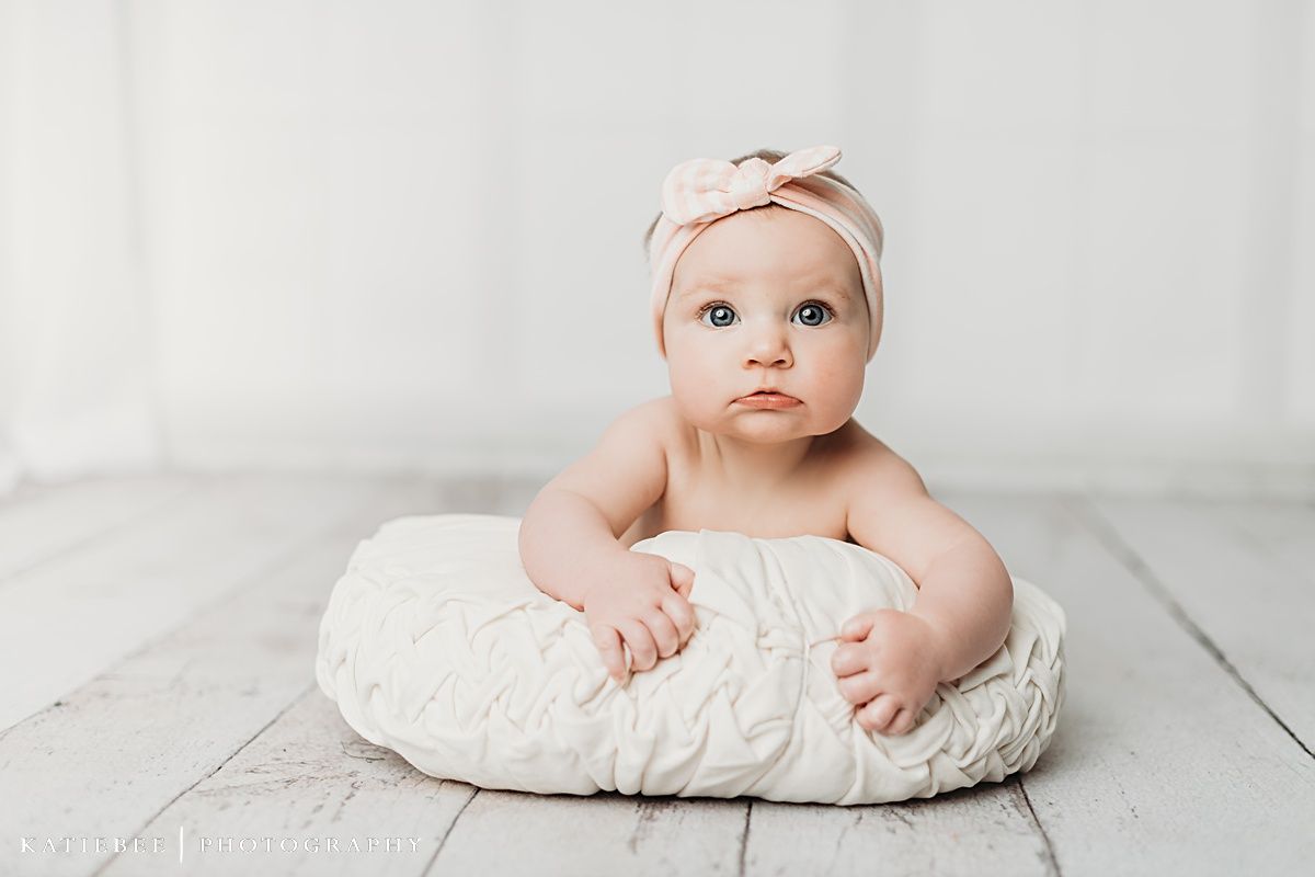 Baby propped on a white cushion against light backdrop during professional photoshoot.