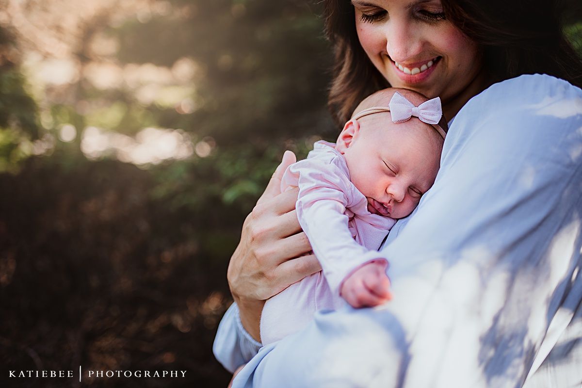 Sunlit portrait of a sleeping infant in pink being held lovingly against light blue clothing.