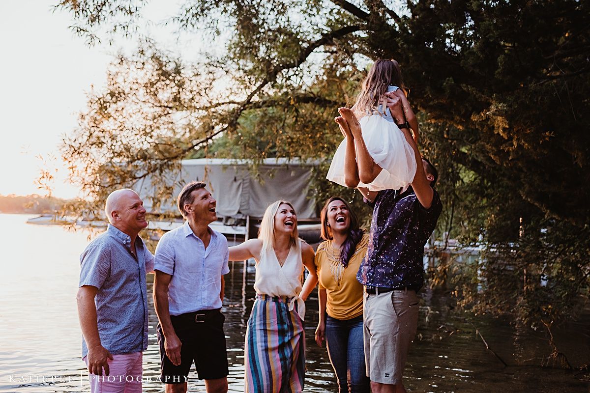 A group enjoying sunset by the lake with a child being lifted in celebration.