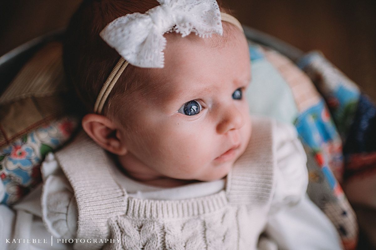 Close-up portrait of a baby wearing a white bow headband and cream-colored outfit.