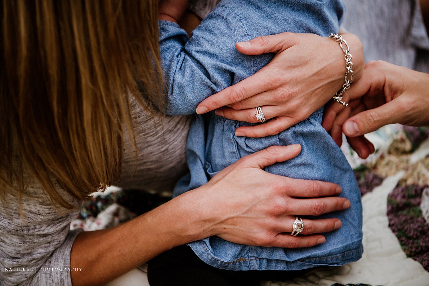 Close up of hands holding and embracing a baby wearing denim clothing.