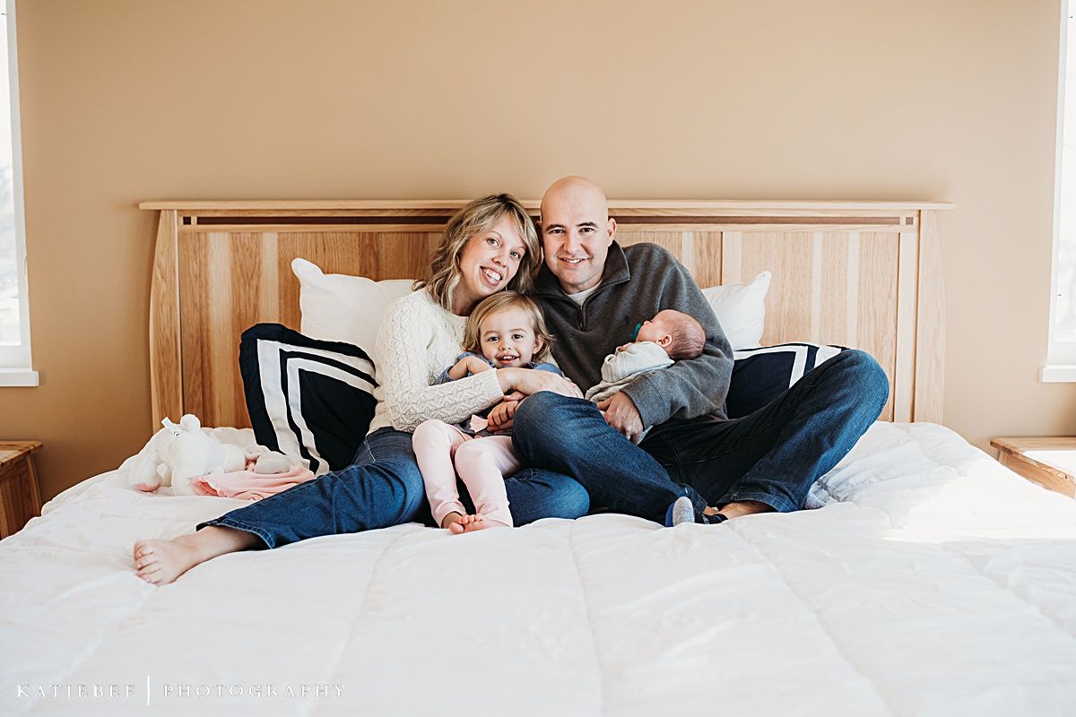 A family of four lounges together on a wooden bed frame with striped pillows.
