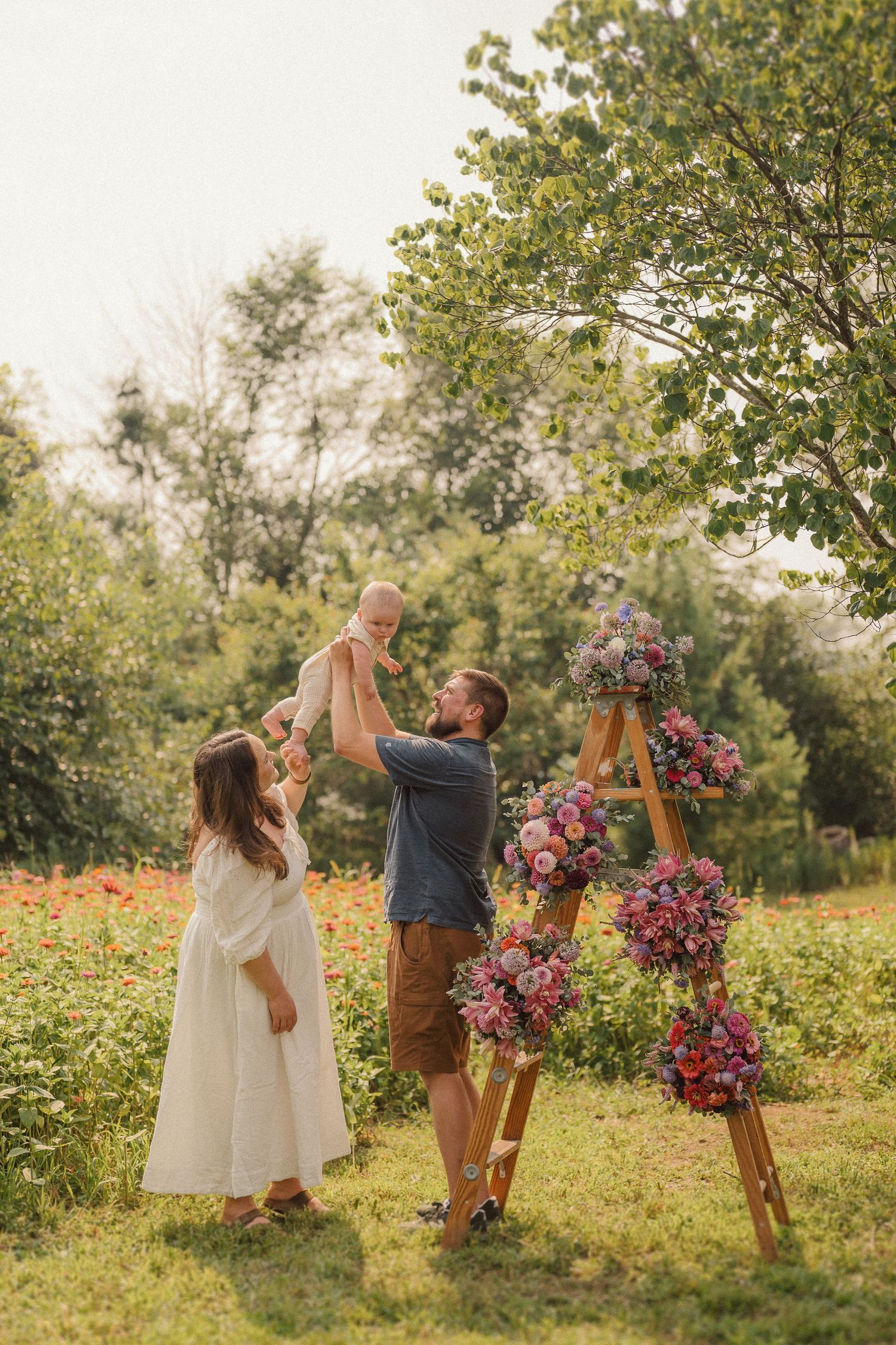 Family enjoying a playful moment together in a garden setting with vibrant pink floral arrangements and trees.