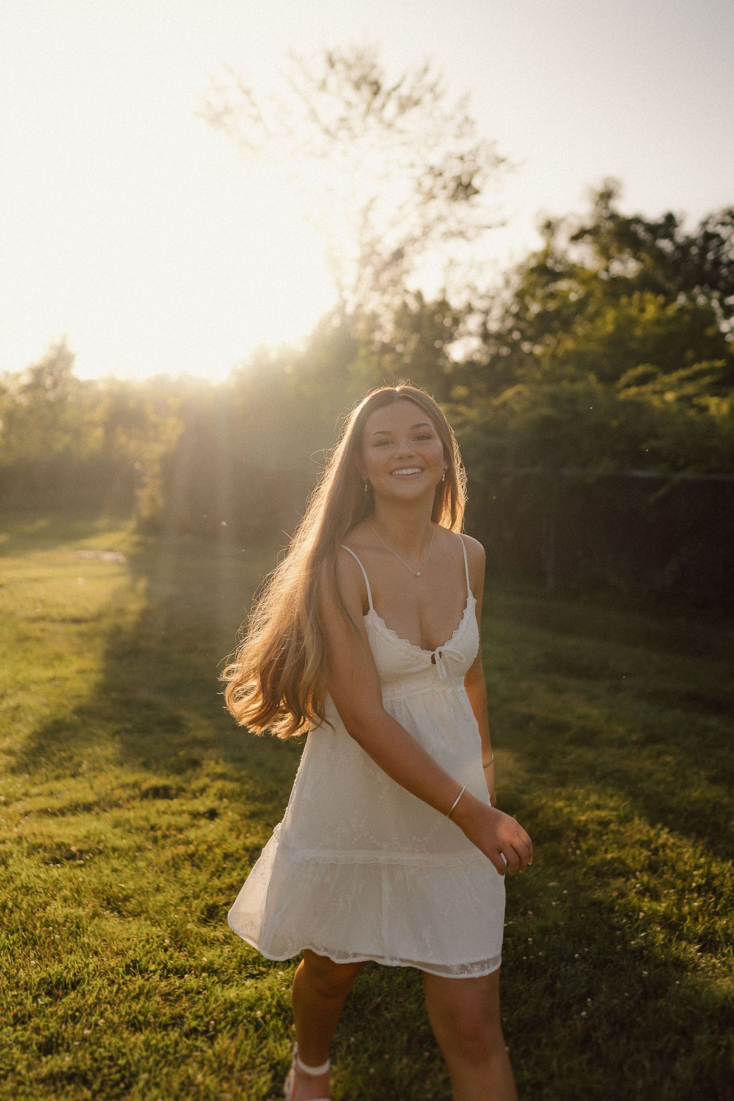 A joyful summer portrait in a sunlit field during golden hour wearing a white dress.