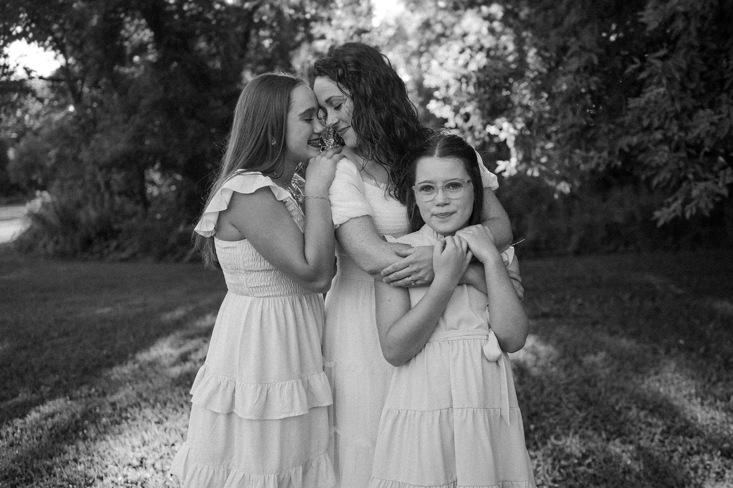 Children in white dresses hold hands while walking through wooded outdoor path in summer.