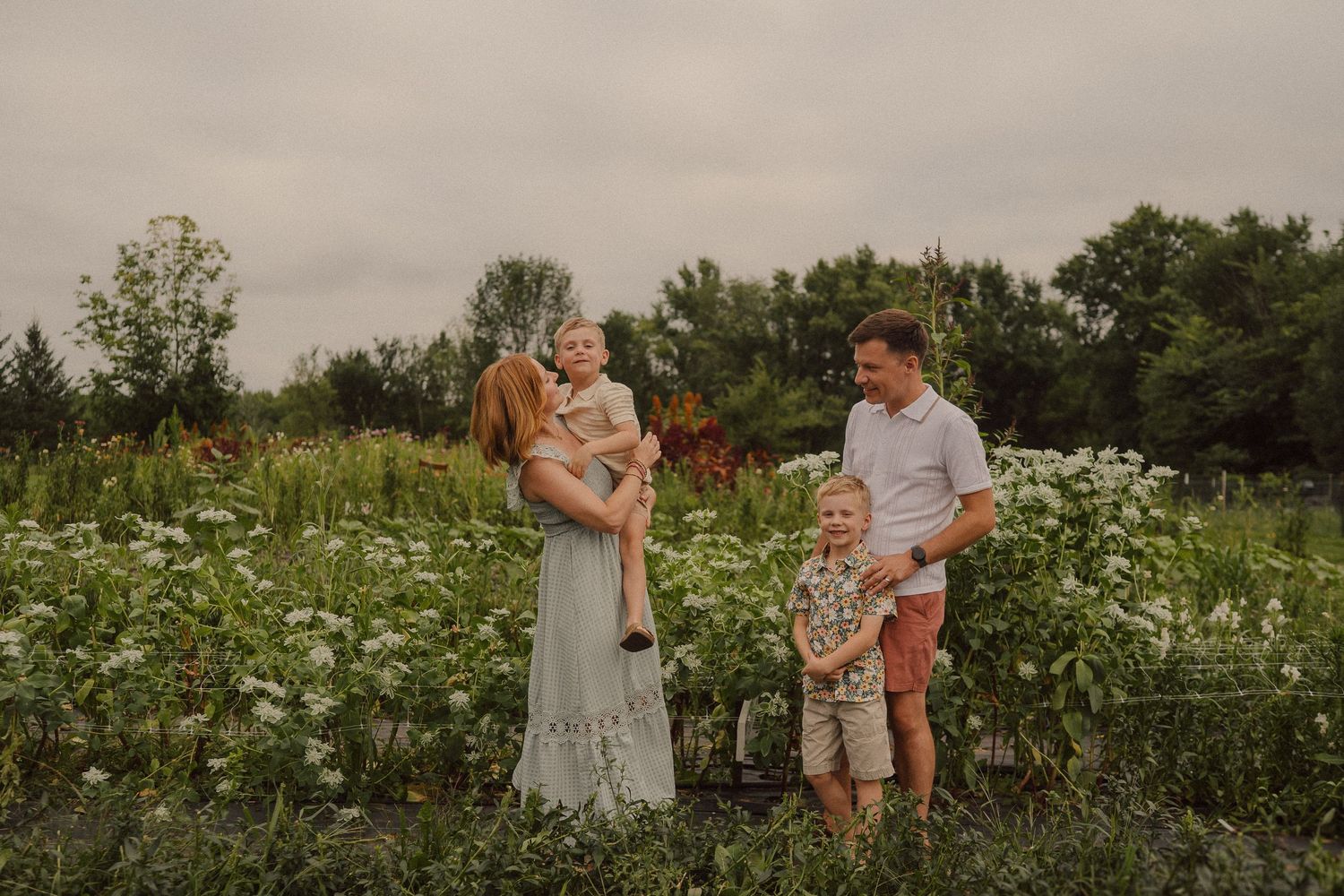 A couple walks together and poses romantically in a blooming meadow field filled with white wildflowers.