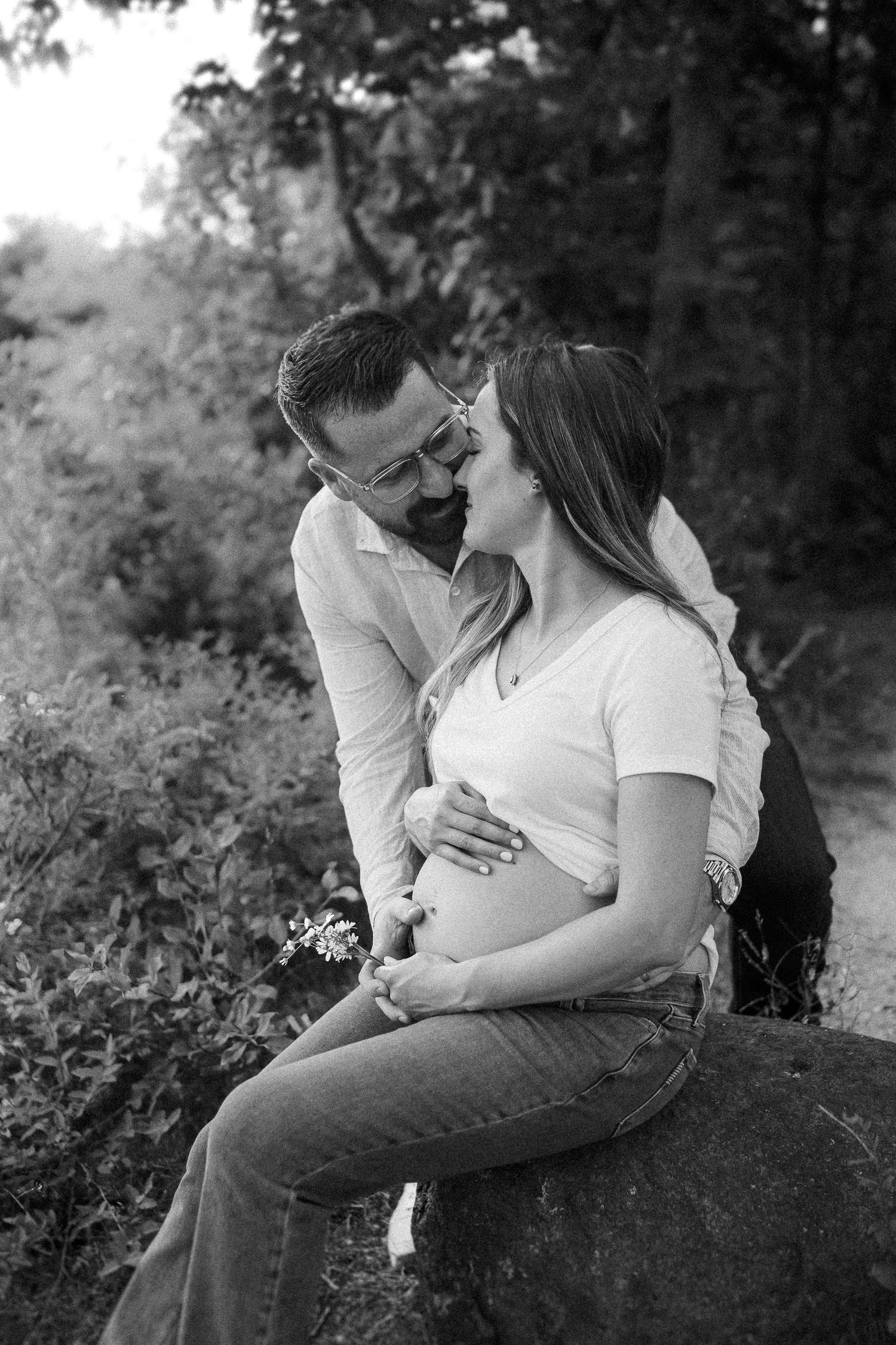 Intimate black and white photos of couple sitting on rock surrounded by nature.