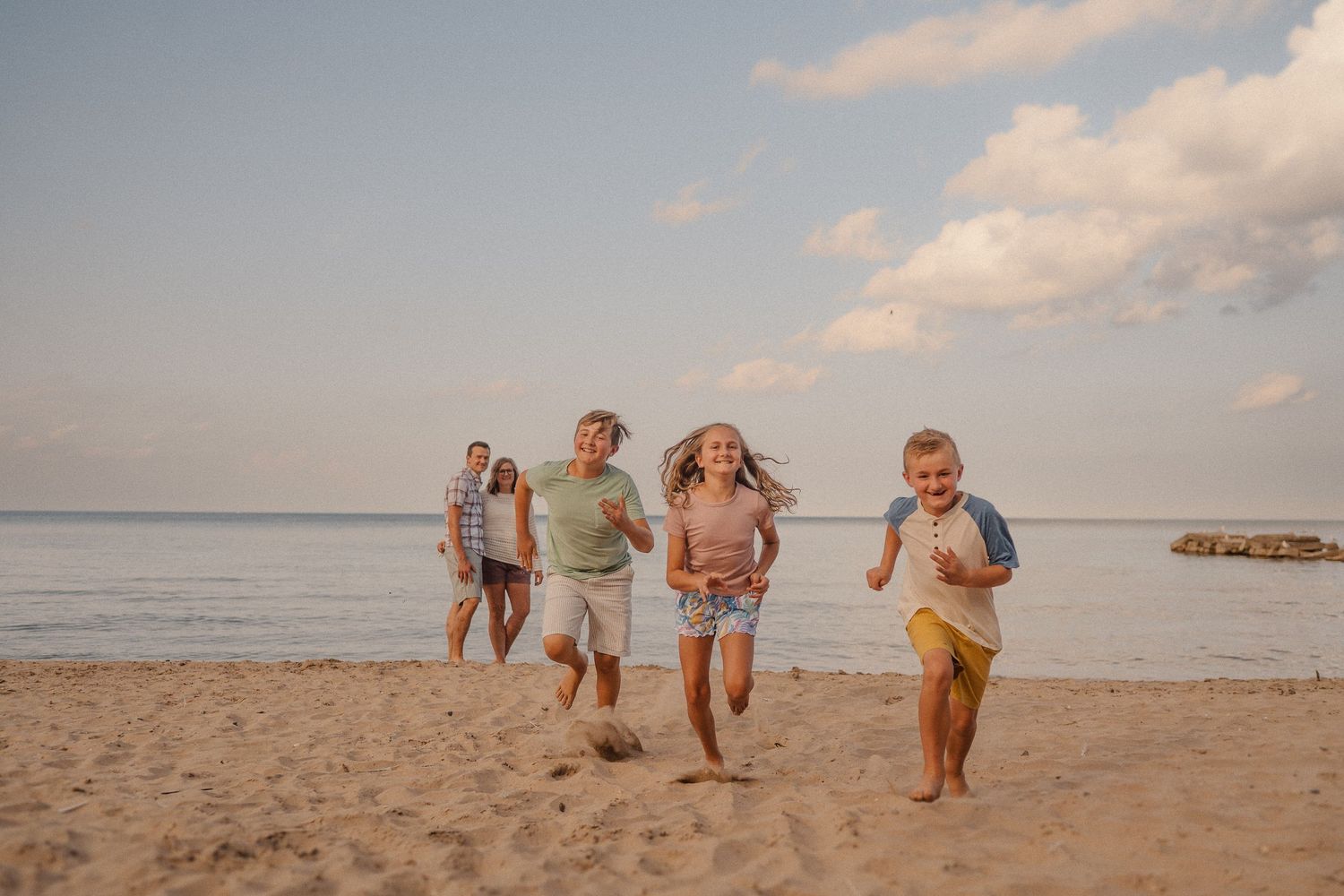 A group plays and jumps together on a sandy beach during sunset, creating joyful silhouettes against the sky.