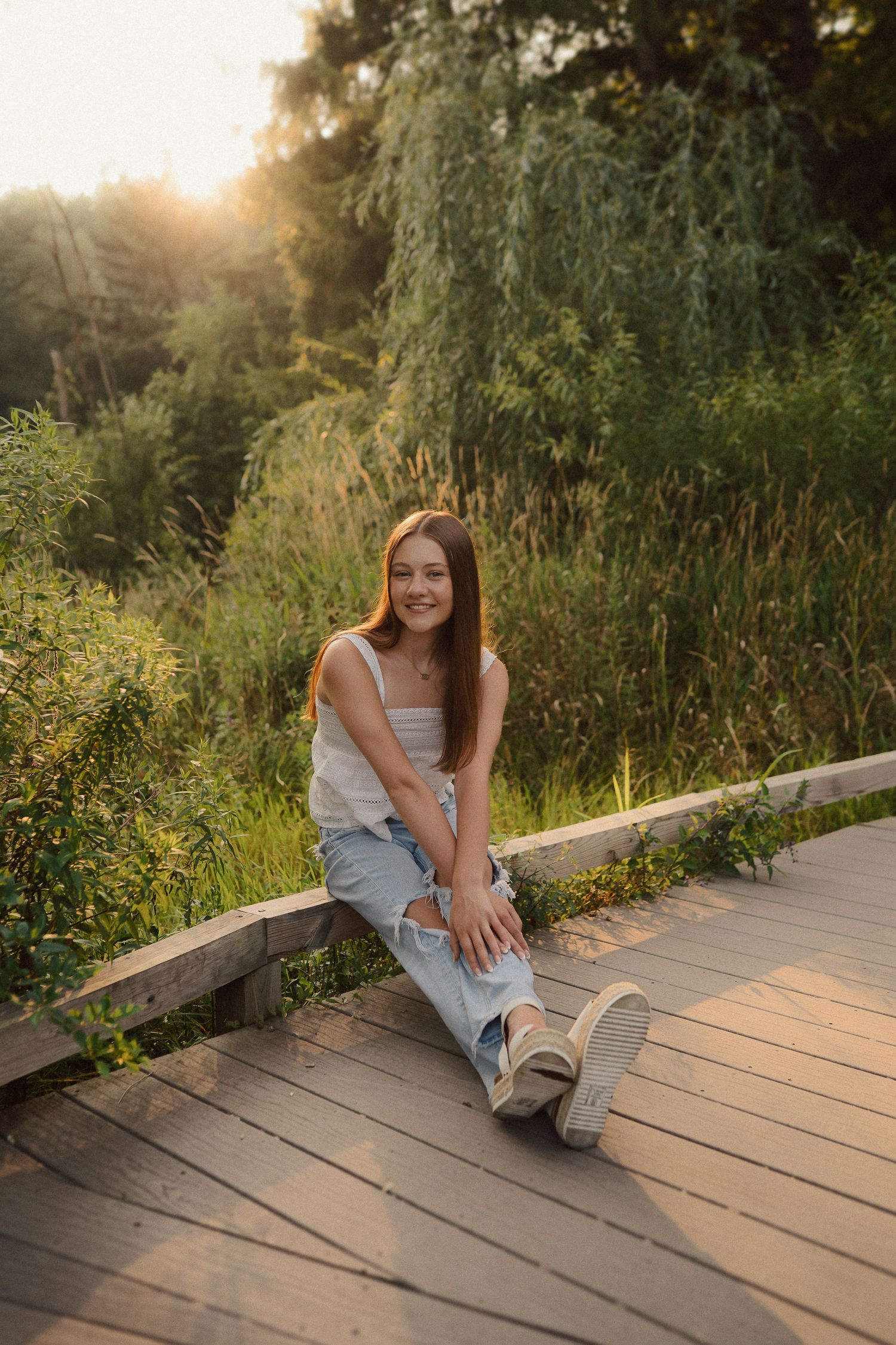 A peaceful summer evening scene on a wooden deck surrounded by lush greenery at sunset.