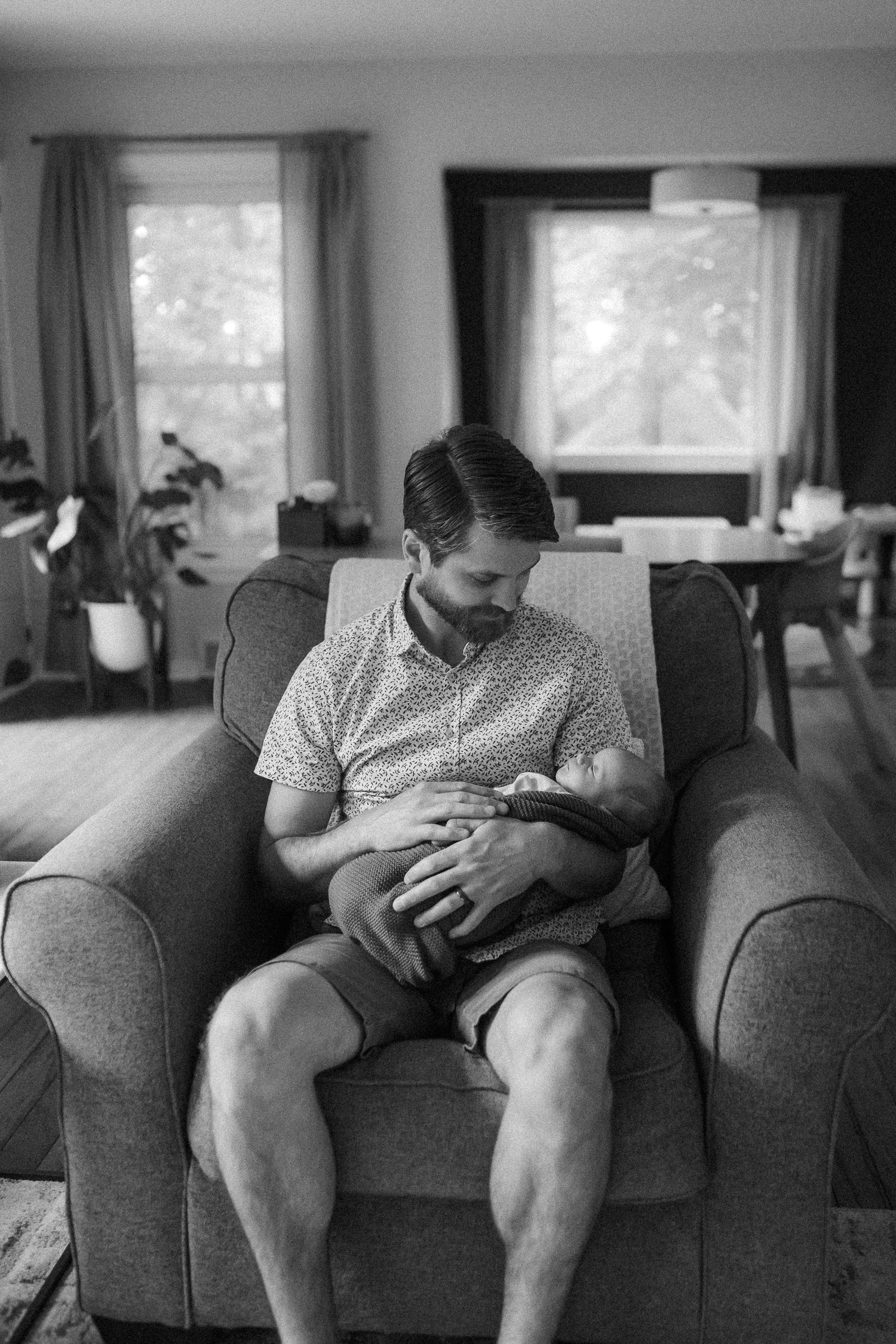 Black and white photo captures intimate parenting moment on grey couch in bright living room.