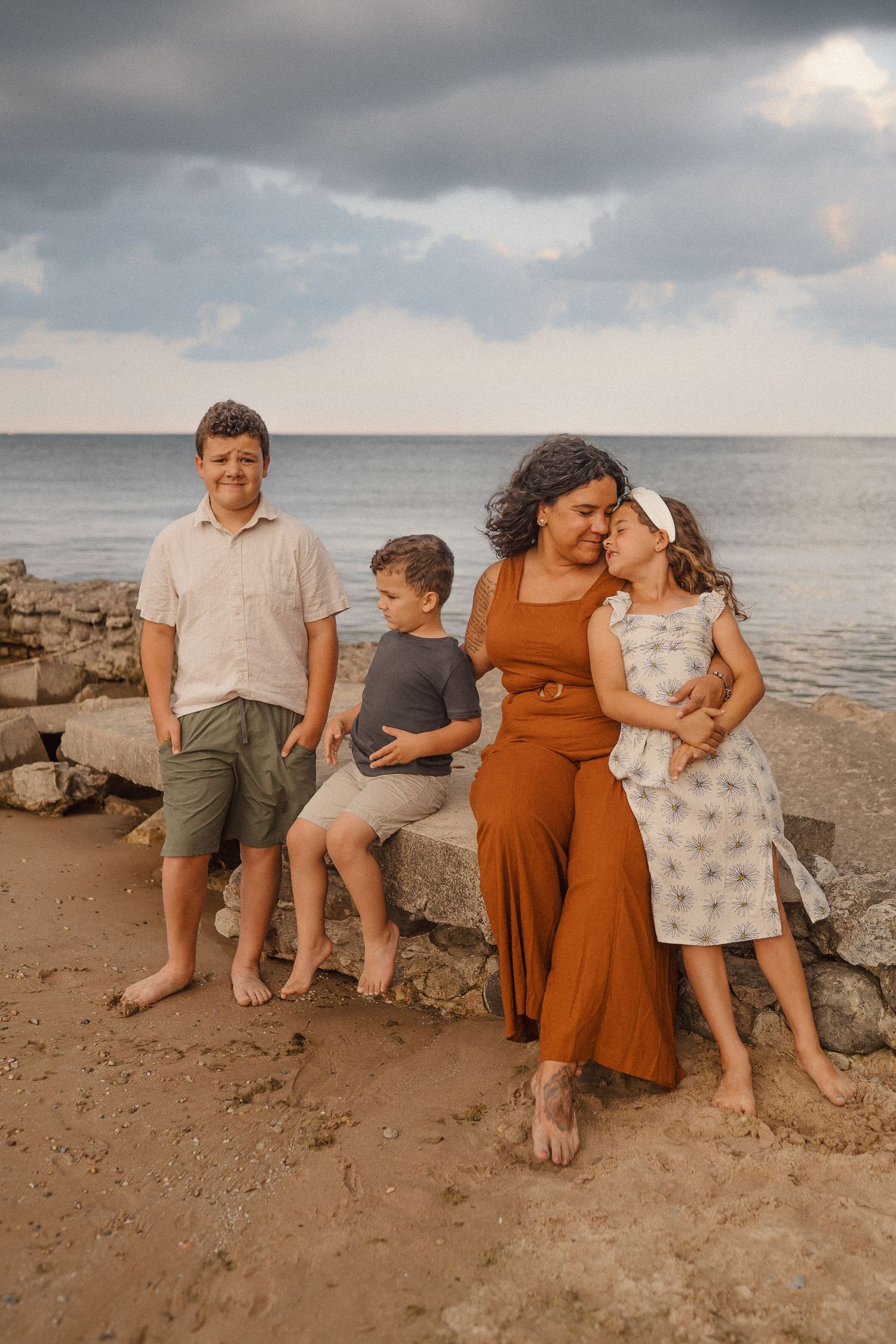 A family shares a tender moment together on a rocky beach at sunset with stormy clouds overhead.
