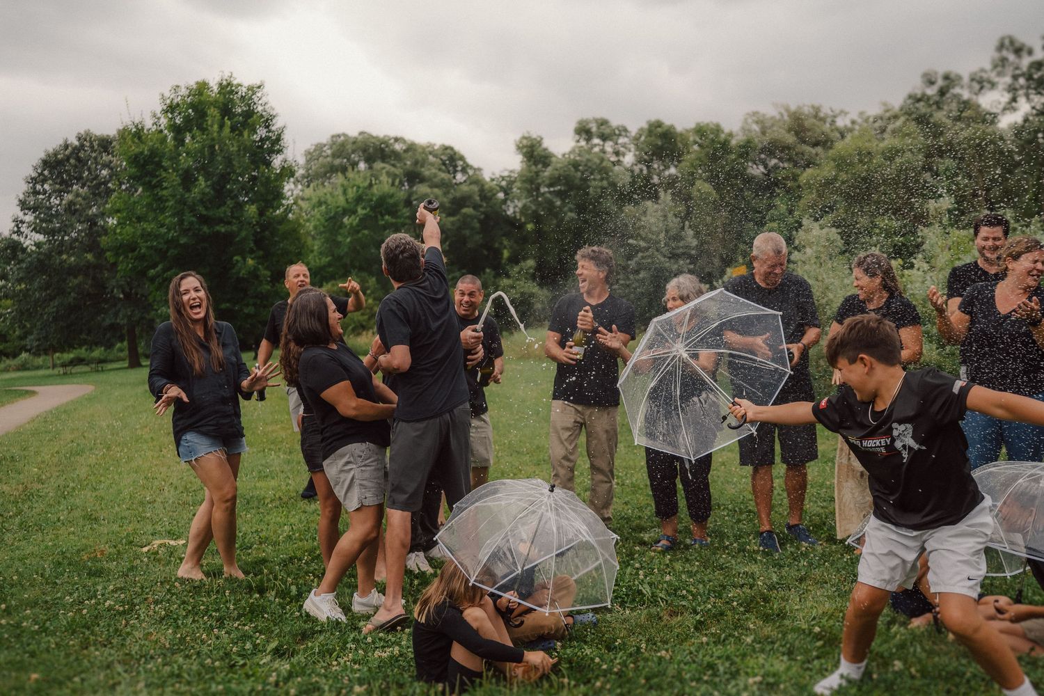 People celebrating outdoors with champagne bottles spraying in the air.