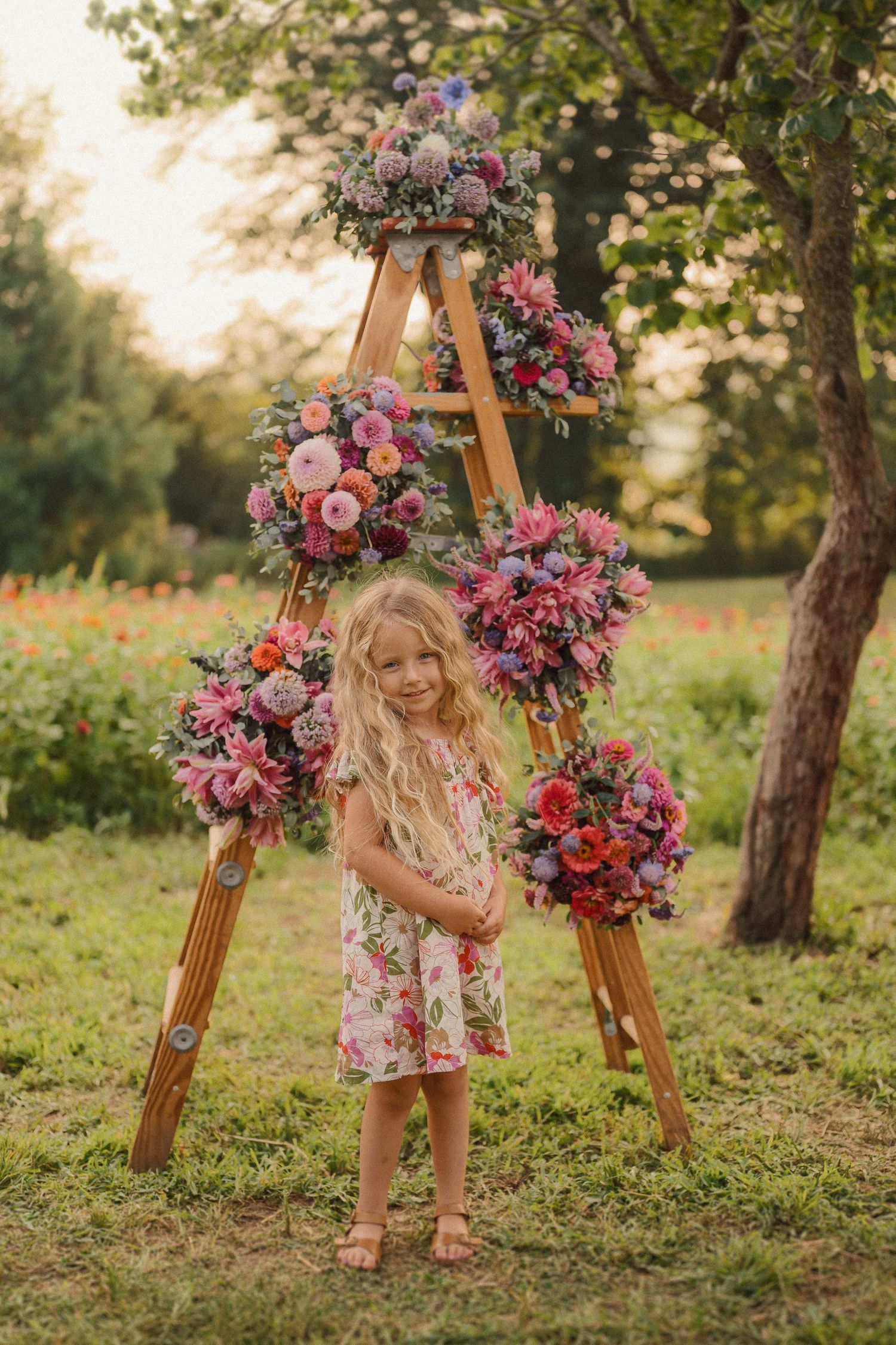 A young child in a floral dress plays near a wooden A-frame decorated with vibrant pink and purple flower arrangements.