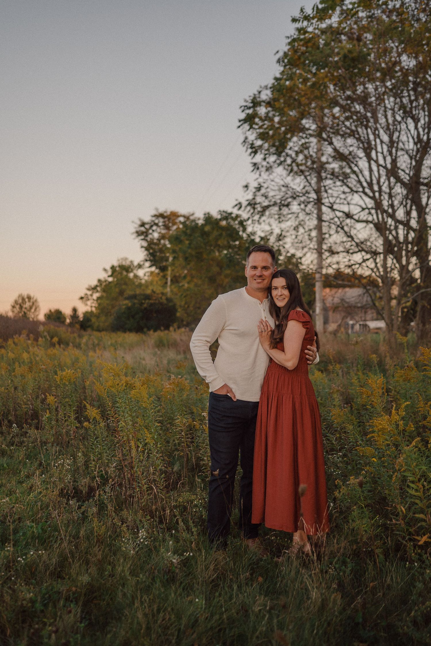 Couple embraces in rustic field during golden hour portrait session.