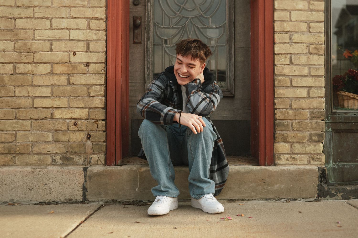 A figure in casual wear sits on stone steps against a brick wall exterior.