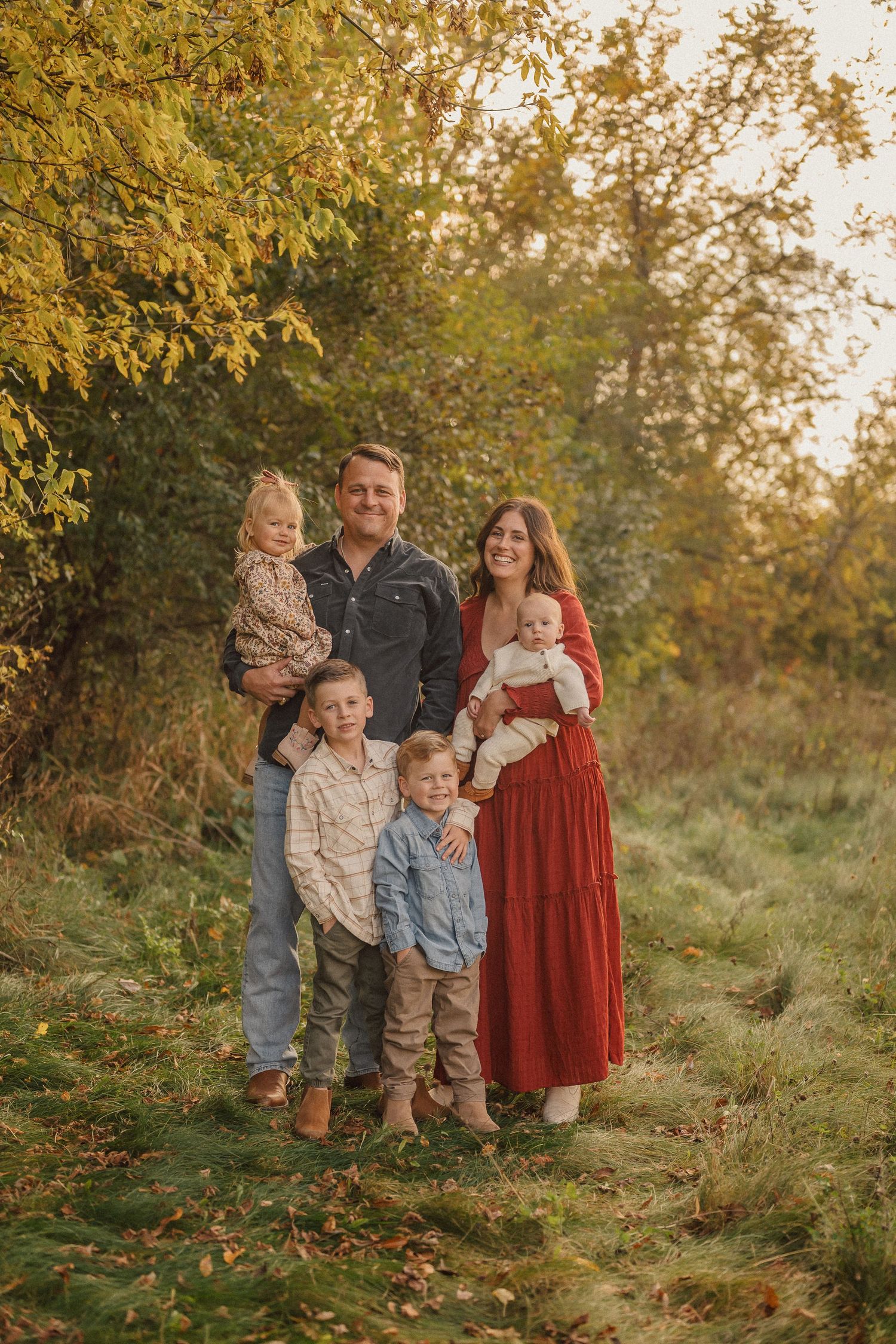 Family poses together outdoors during golden hour autumn photoshoot in casual attire.