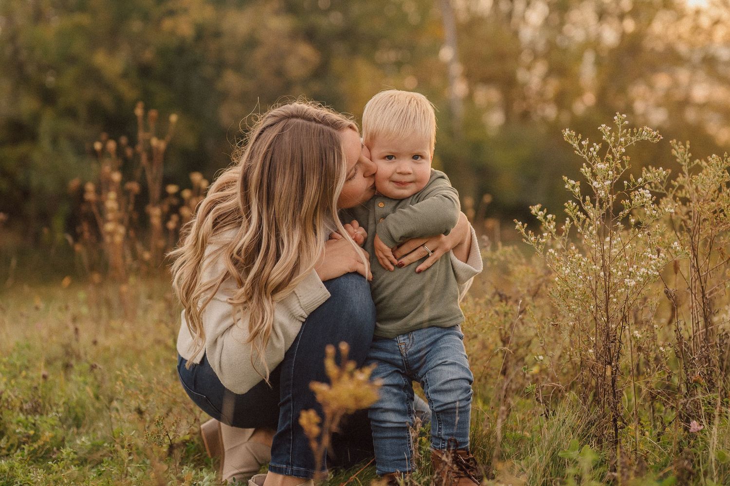 Parents holding toddler's hands while walking through tall grass at sunset.