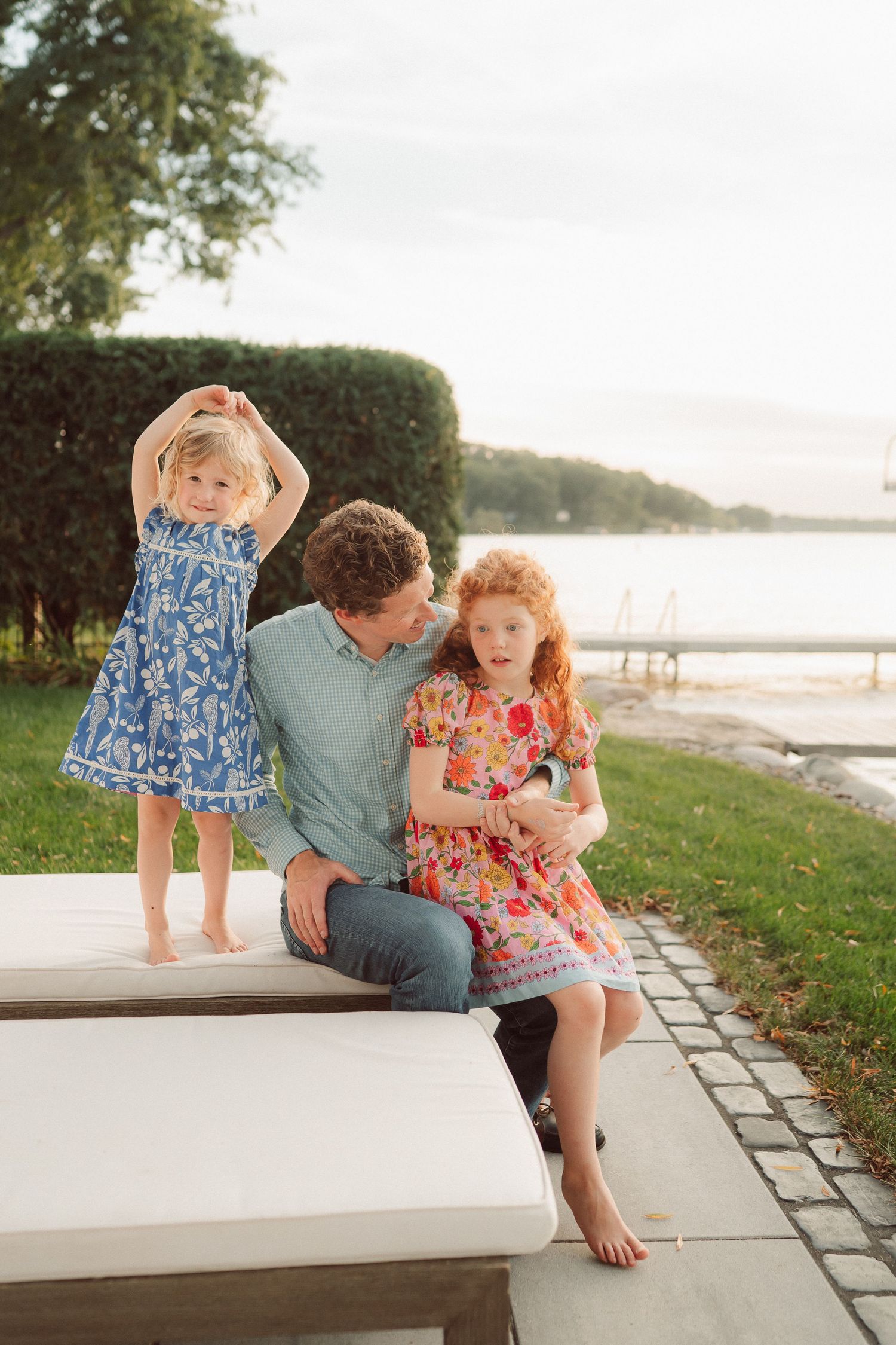 Family sitting together on white stone benches by a waterfront park at sunset.