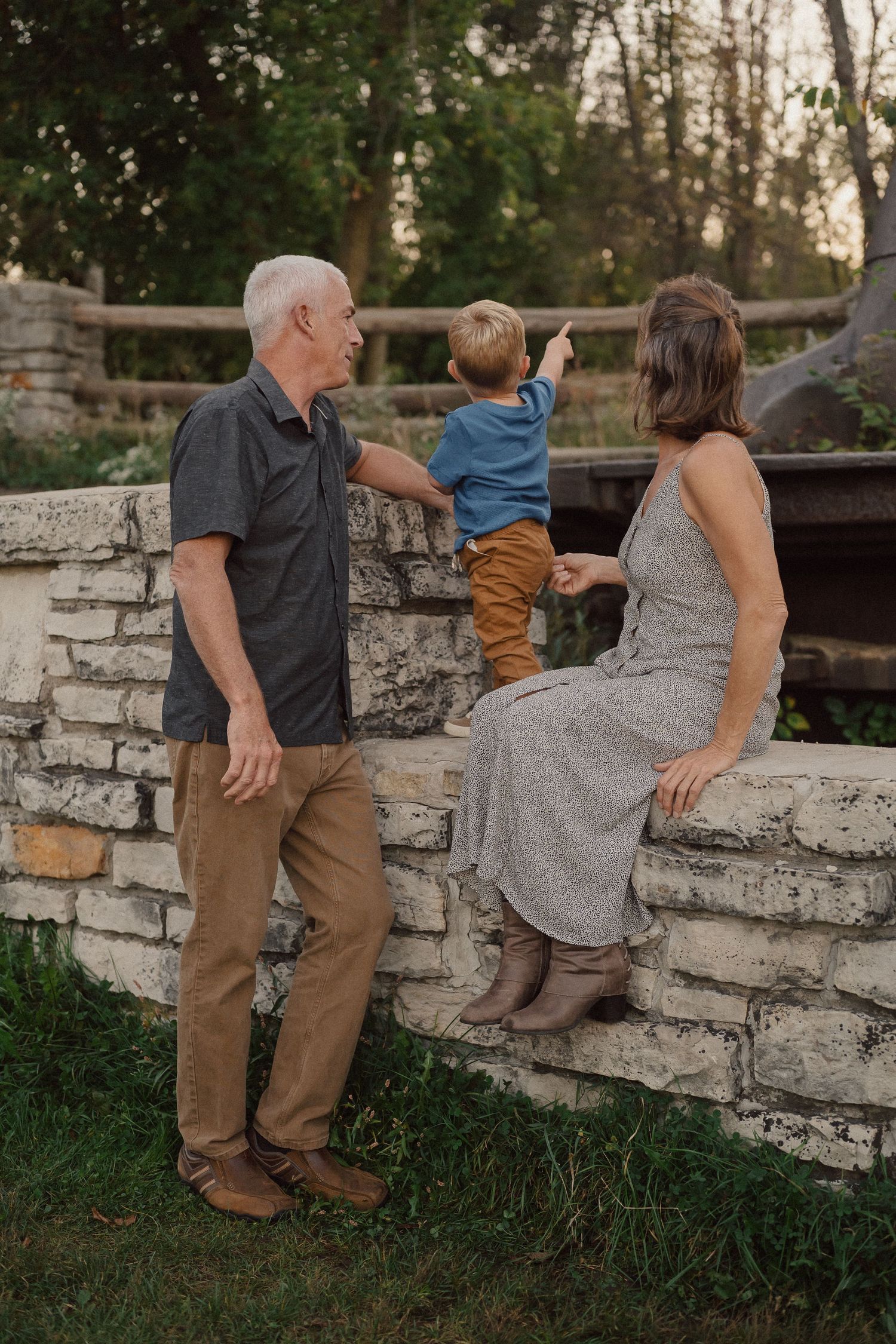 Family sitting together on a rustic stone wall during a casual outdoor photo session at sunset.
