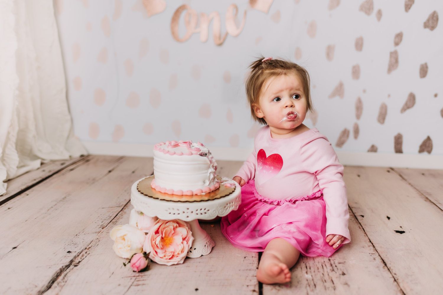Celebration scene with pink cake and floral decor against white polka dot backdrop.