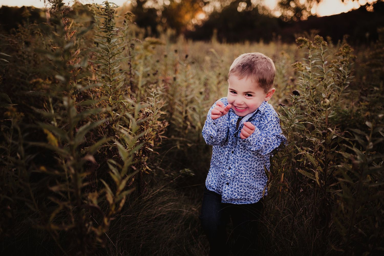 Small child in patterned shirt standing among tall plants at sunset.