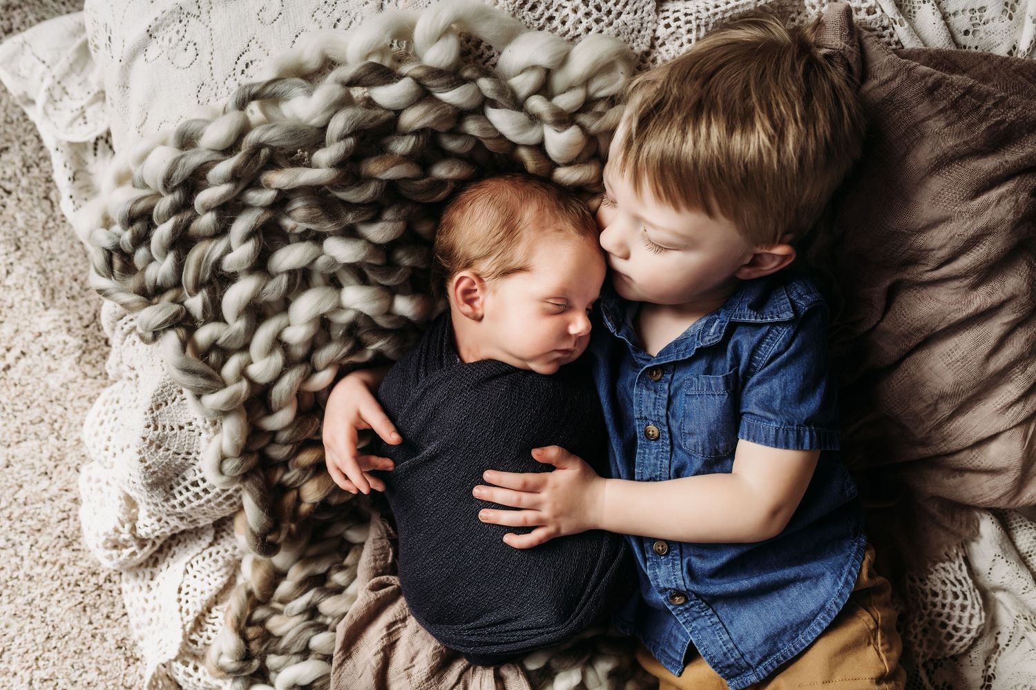 Two small children cuddle on a cozy chunky knit blanket while sharing a tender moment together.