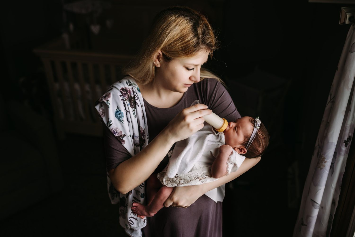 Caregiver in floral dress tends to newborn in moody lighting.