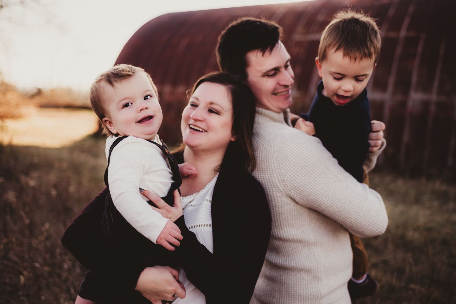 Happy family portrait outdoors at sunset with rustic barn backdrop.
