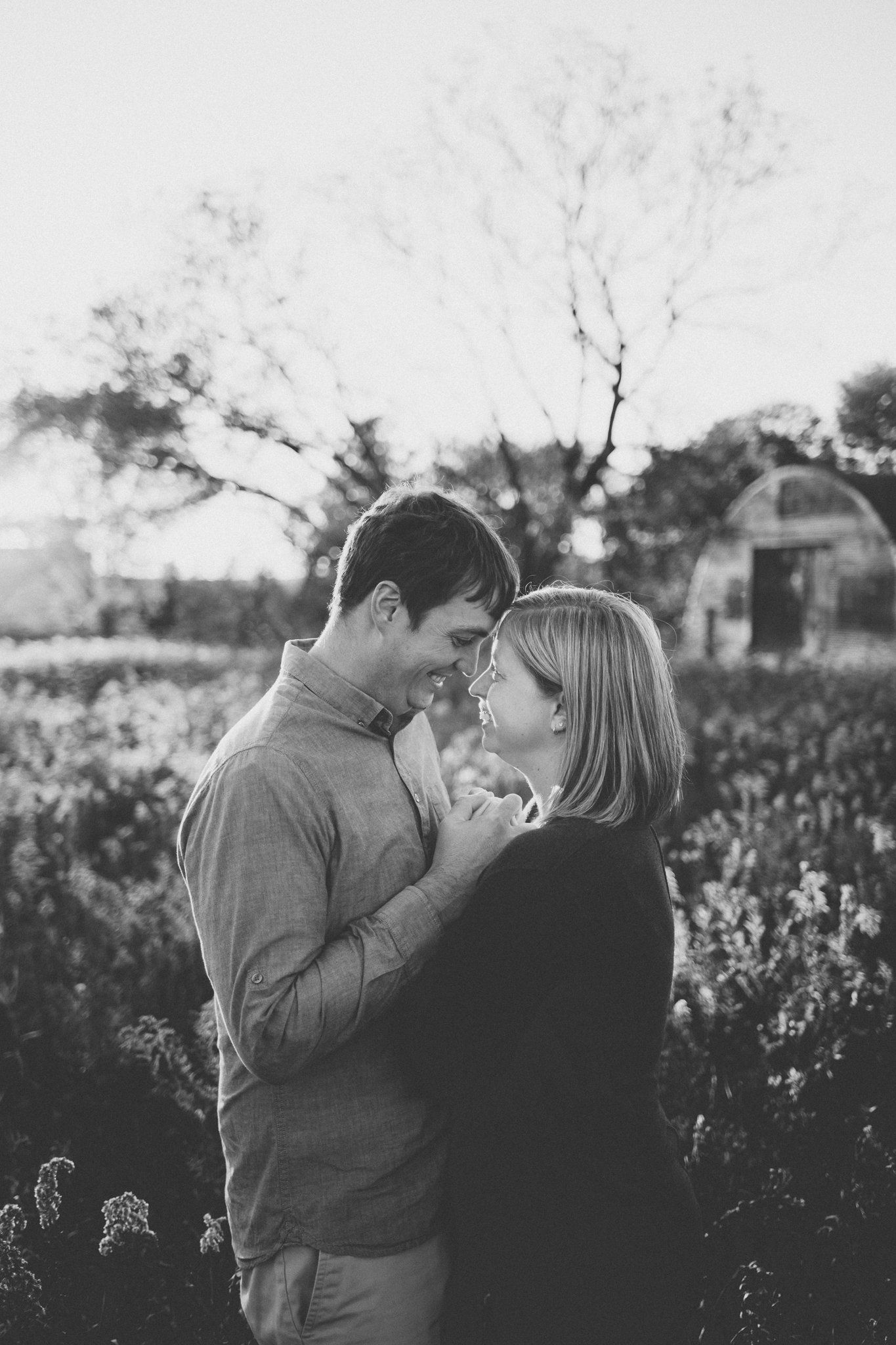 A romantic black and white portrait of a couple in a rustic outdoor setting.