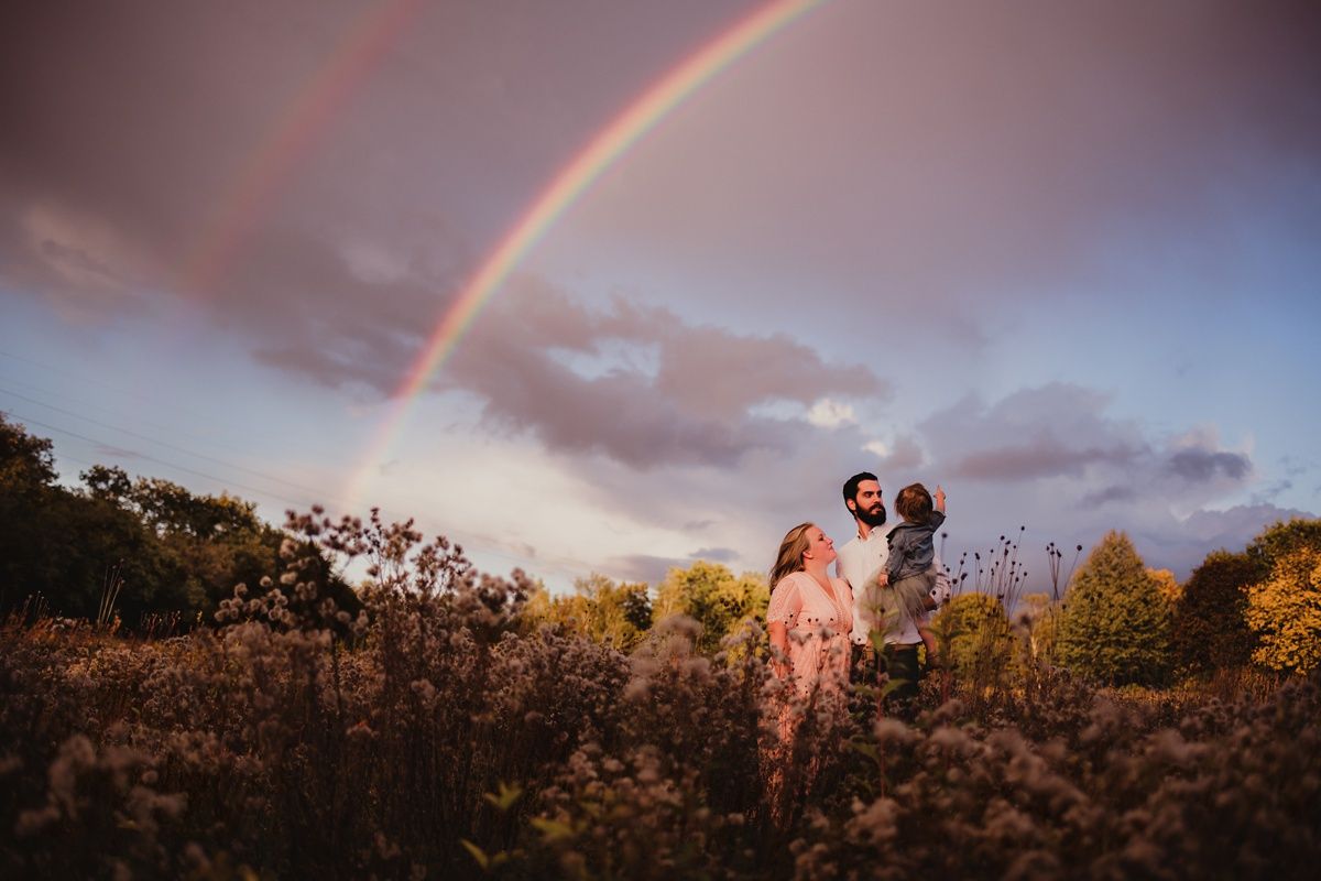 Double rainbow arches over a romantic evening photoshoot in a rustic field.