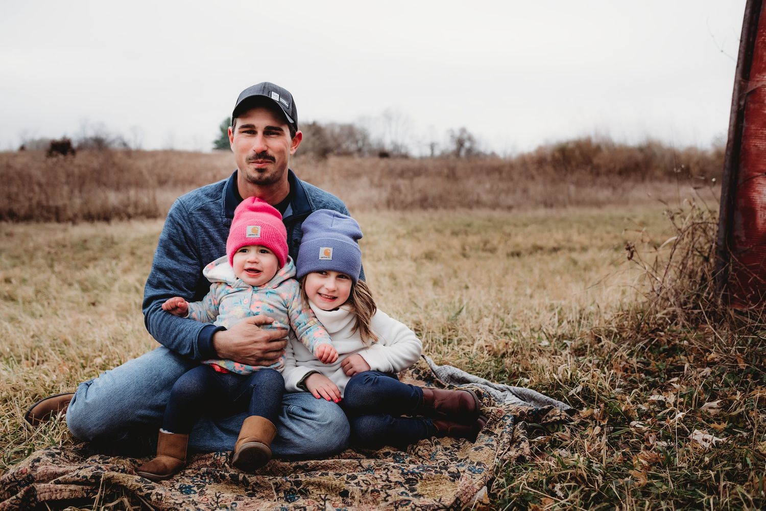 Casual outdoor portrait showing family sitting together in a rural field.