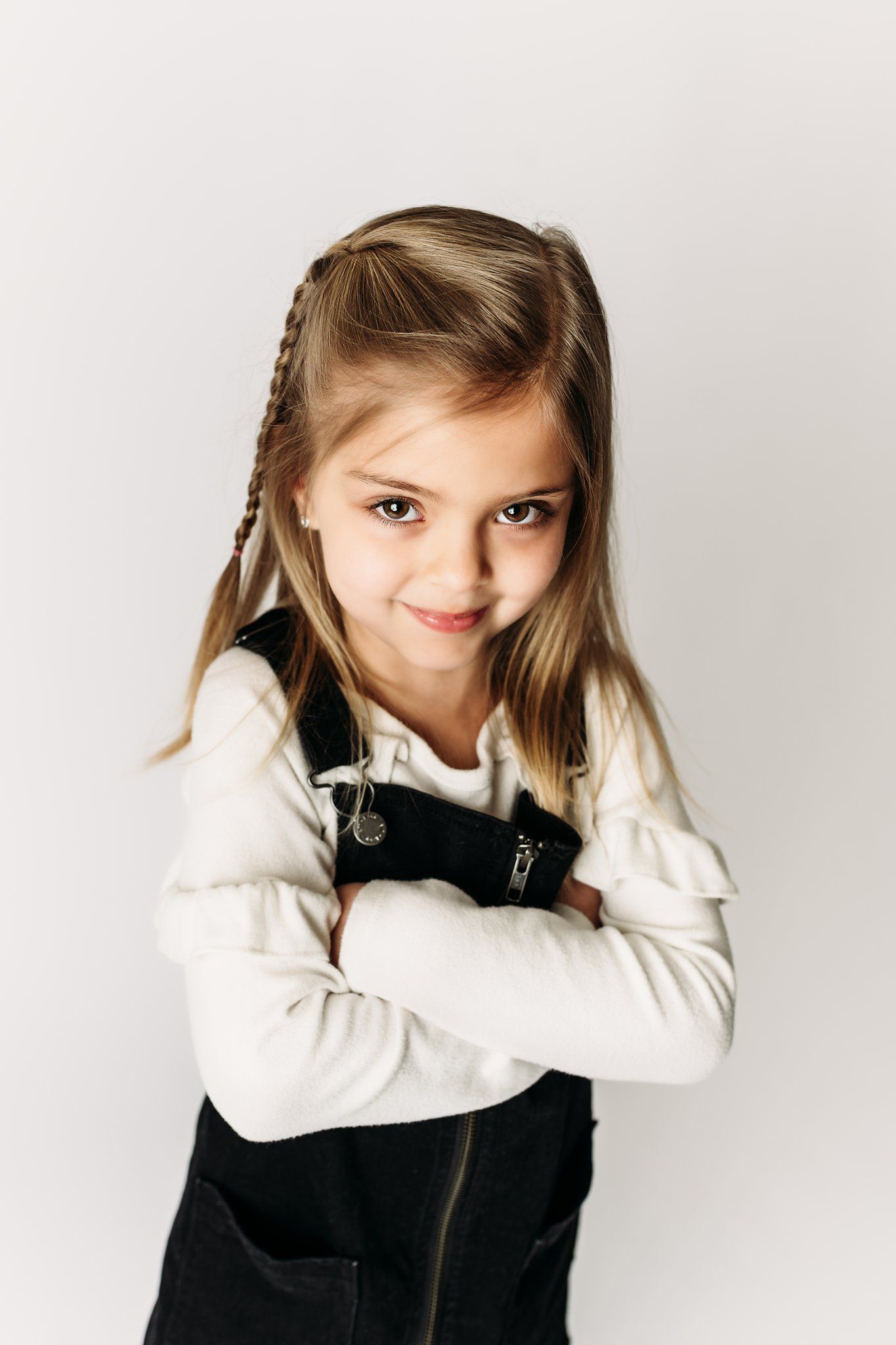 Portrait of child with braided hair wearing black jumper dress and white long sleeve top.