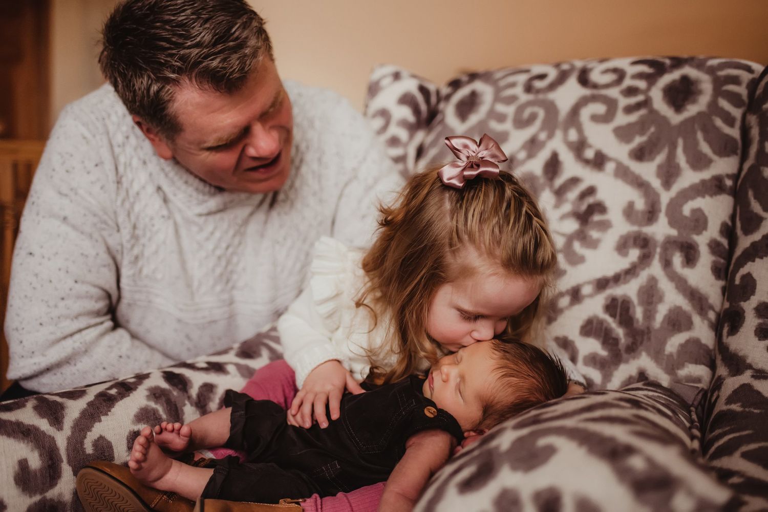 Sweet family moment on a patterned couch showing gentle interaction with a sleeping infant.