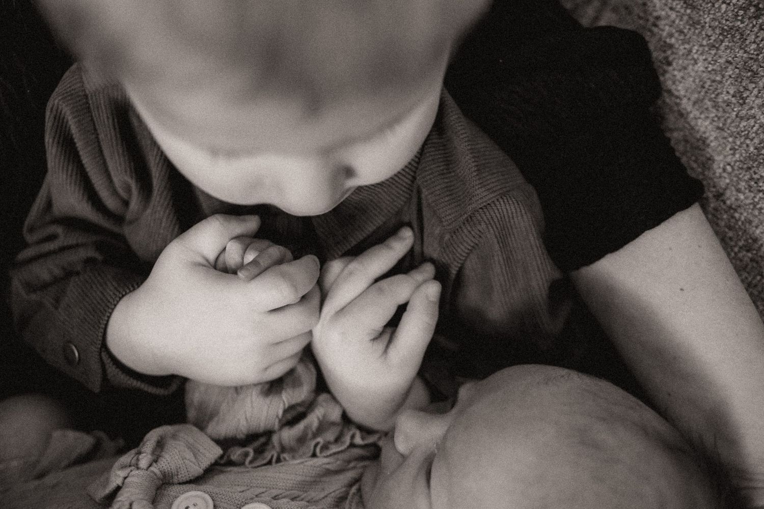 Black and white photo showing tender moment between parent and newborn baby in soft lighting.