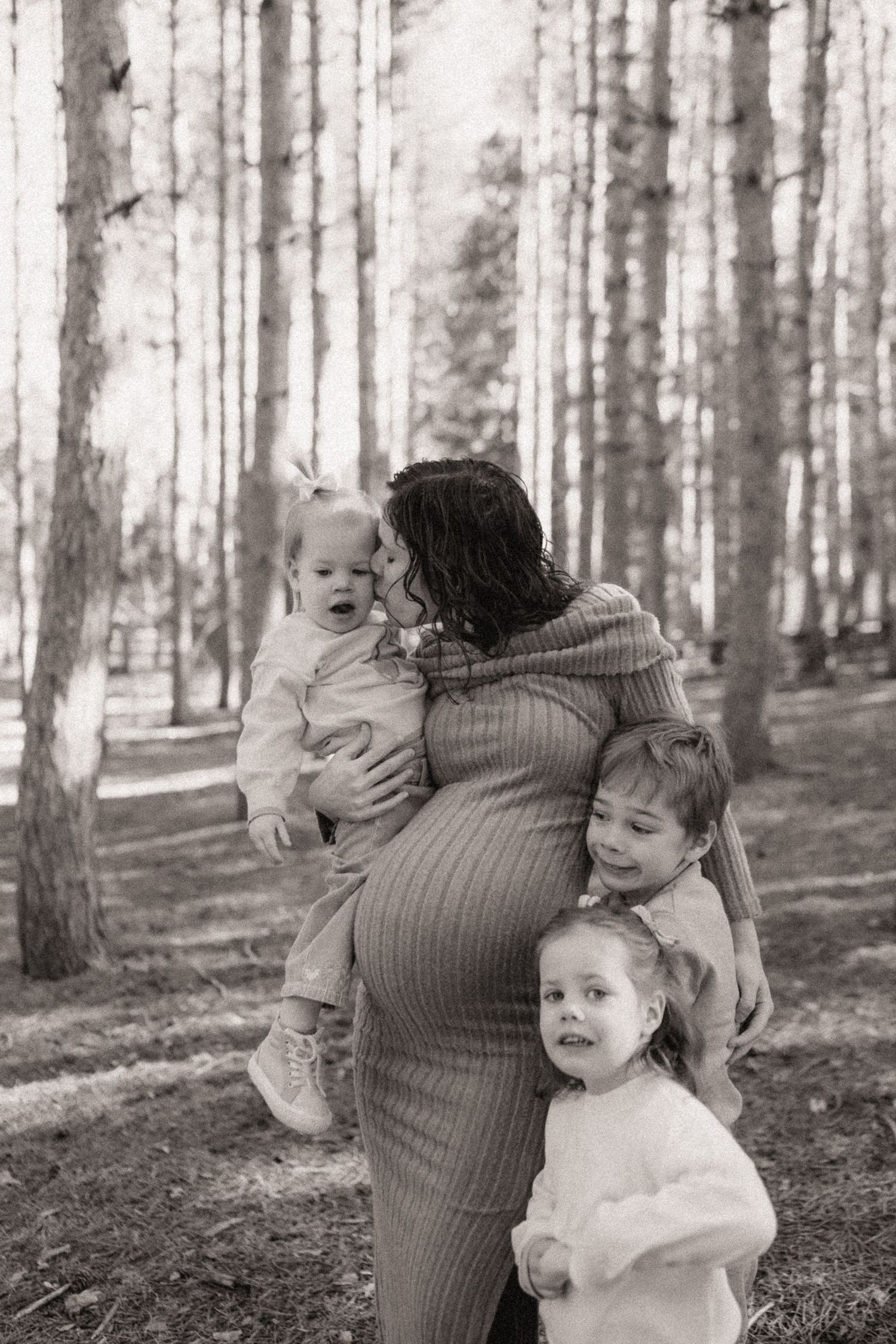 A heartwarming family moment captured in black and white among tall pine trees.