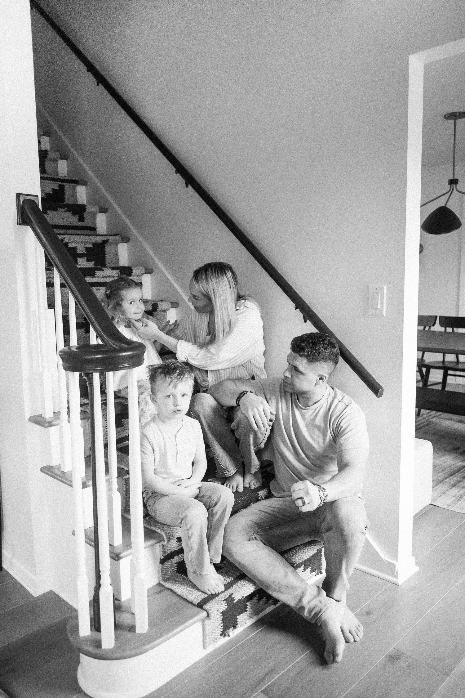 Black and white photo of young family sitting together on home staircase in candid lifestyle portrait.