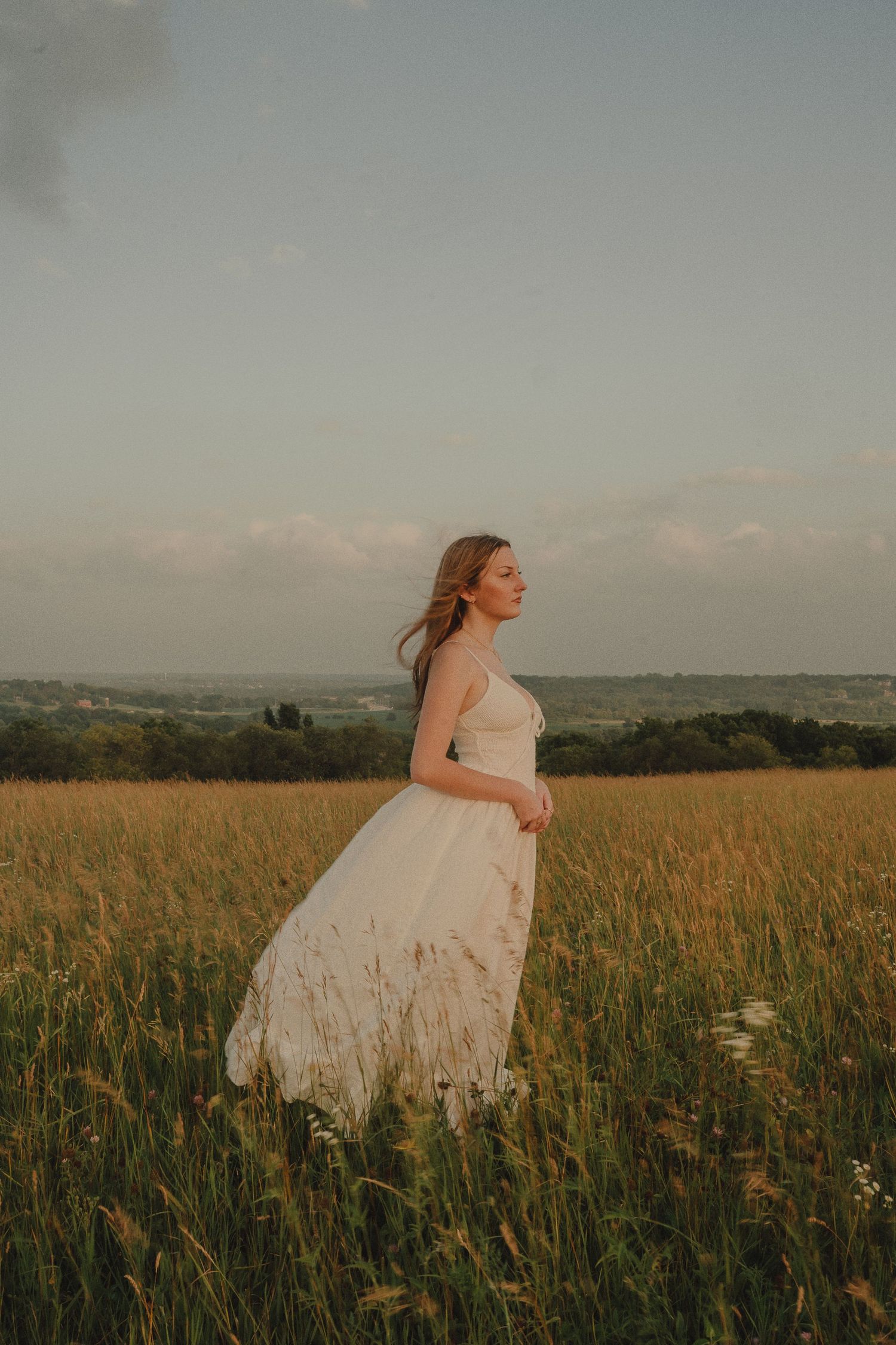 A woman in a flowing white dress stands gracefully in a golden field at sunset.