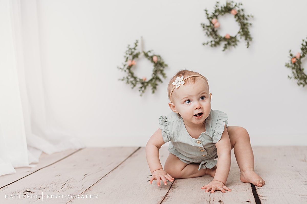 Baby in floral crown with delicate hair bow against white background.