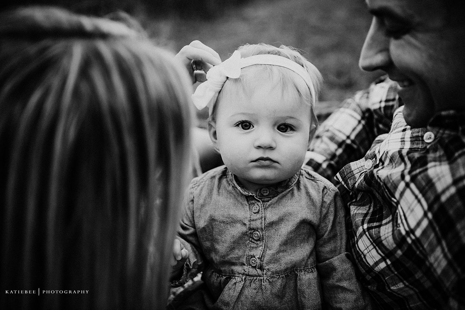 Striking black and white portrait of a baby in a denim dress and white headband.