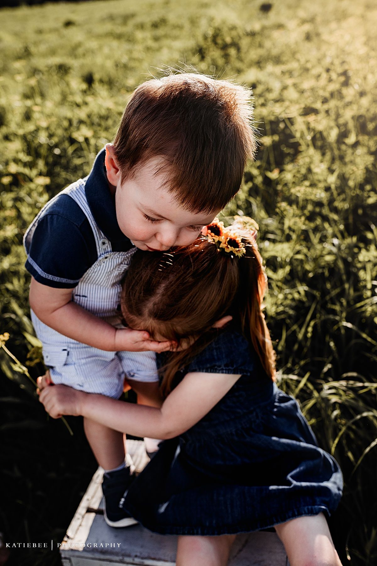 Two children sharing a sweet embrace while sitting outdoors in a golden field.