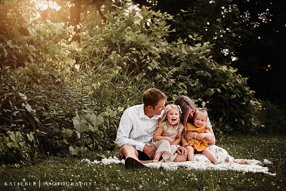 Family laughing together while sitting on blanket outdoors at sunset.