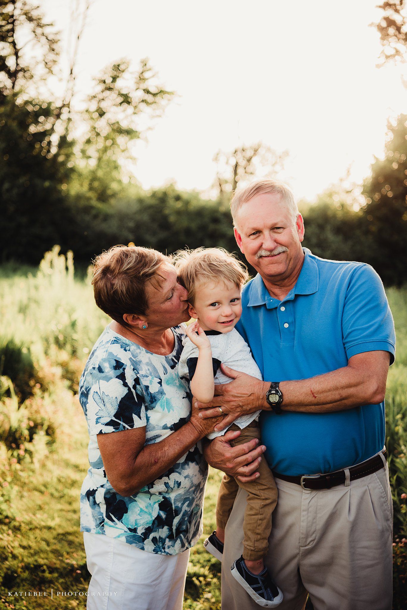 Three generations share a loving embrace in an outdoor setting at sunset.