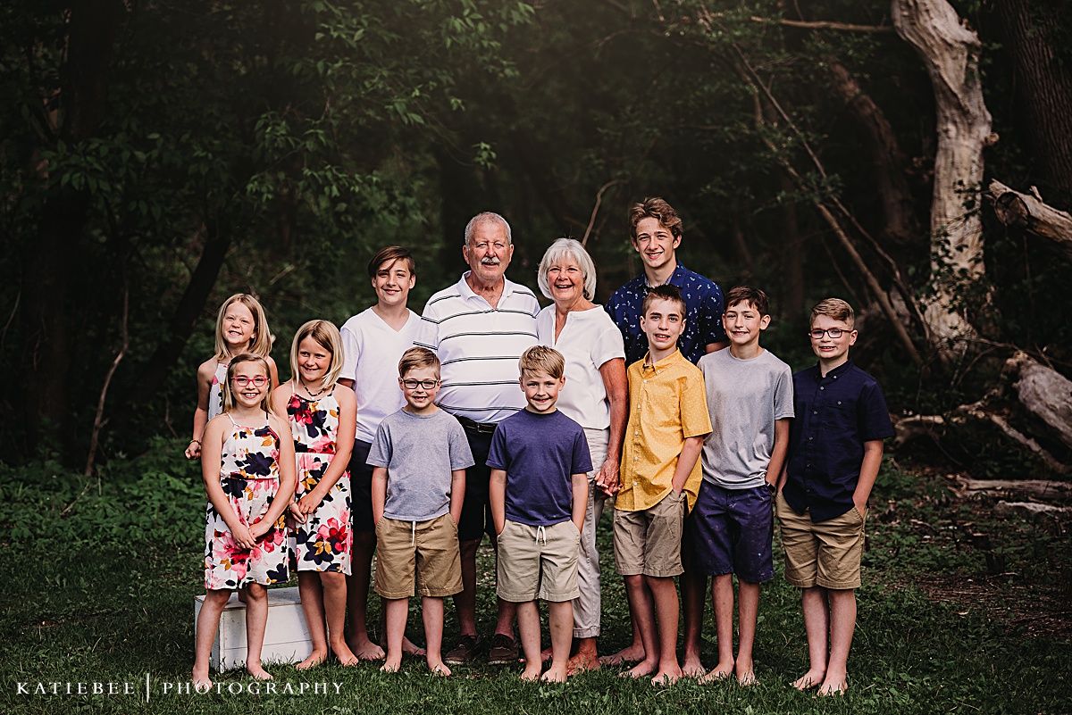 Extended family portrait outdoors with multiple generations wearing coordinated casual attire.