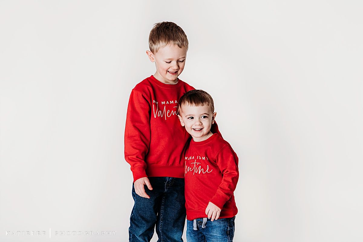 Two posing together in matching red valentine sweaters and jeans against white background.