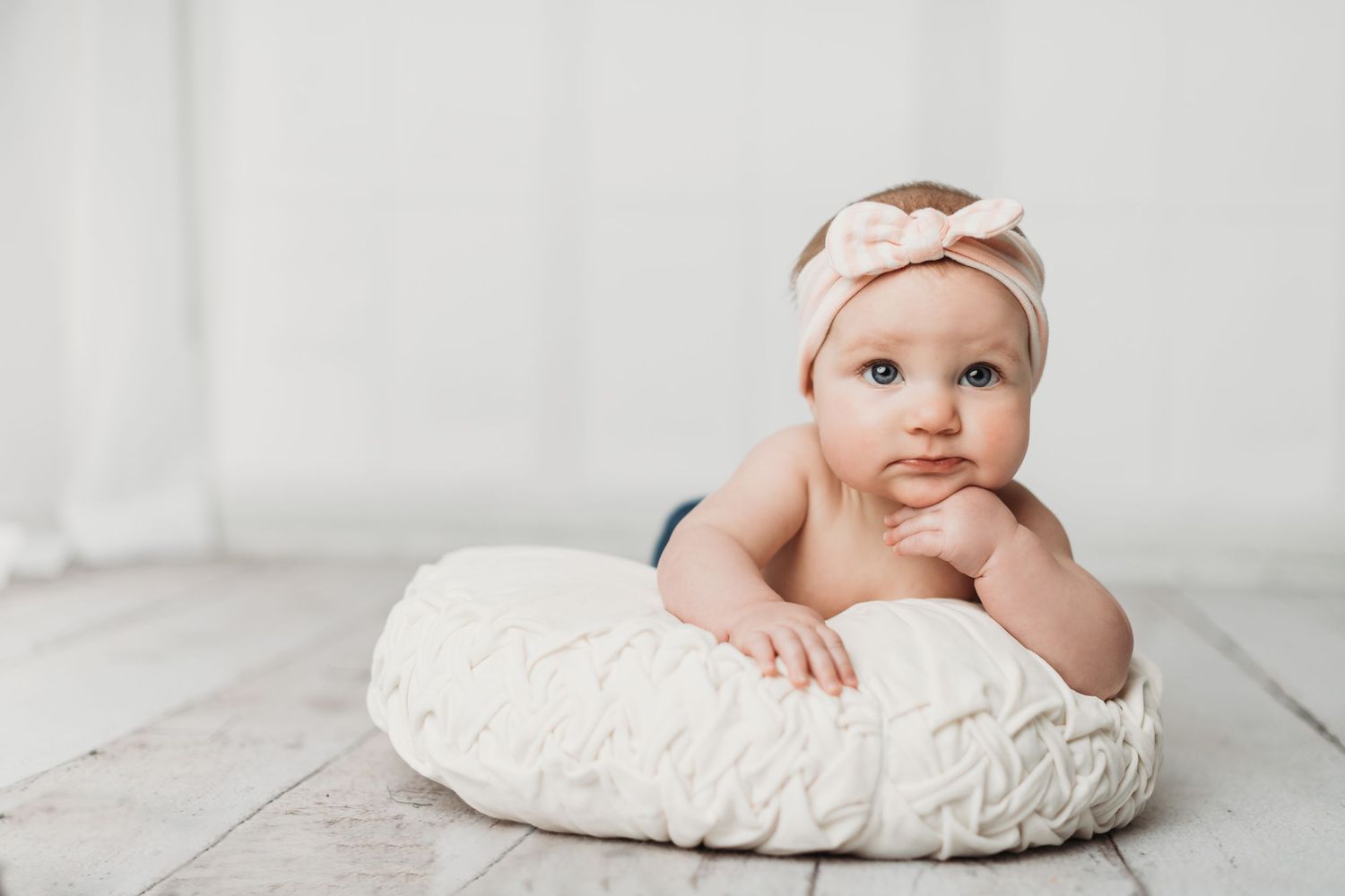 Baby in white headband lying on textured white pillow against light background.