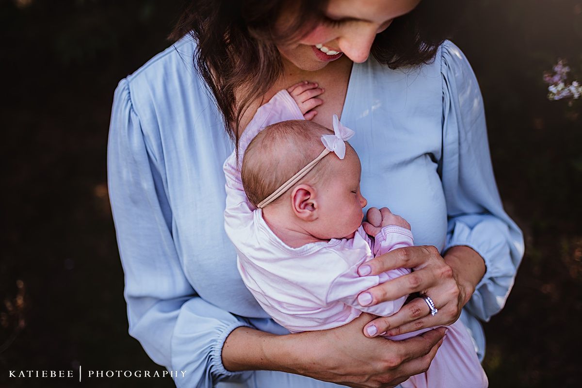 Sweet outdoor portrait of an infant in pink and white being cradled in a light blue top.