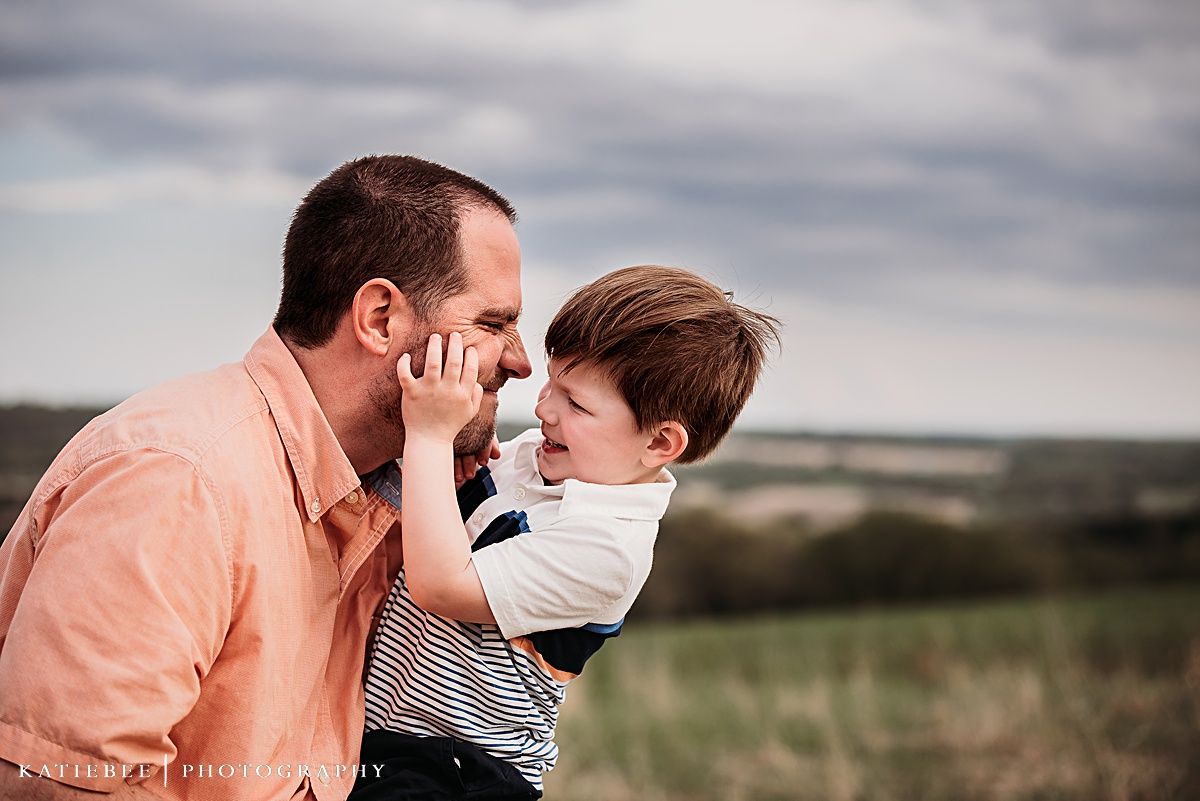 A playful interaction between parent and child against a cloudy rural landscape.