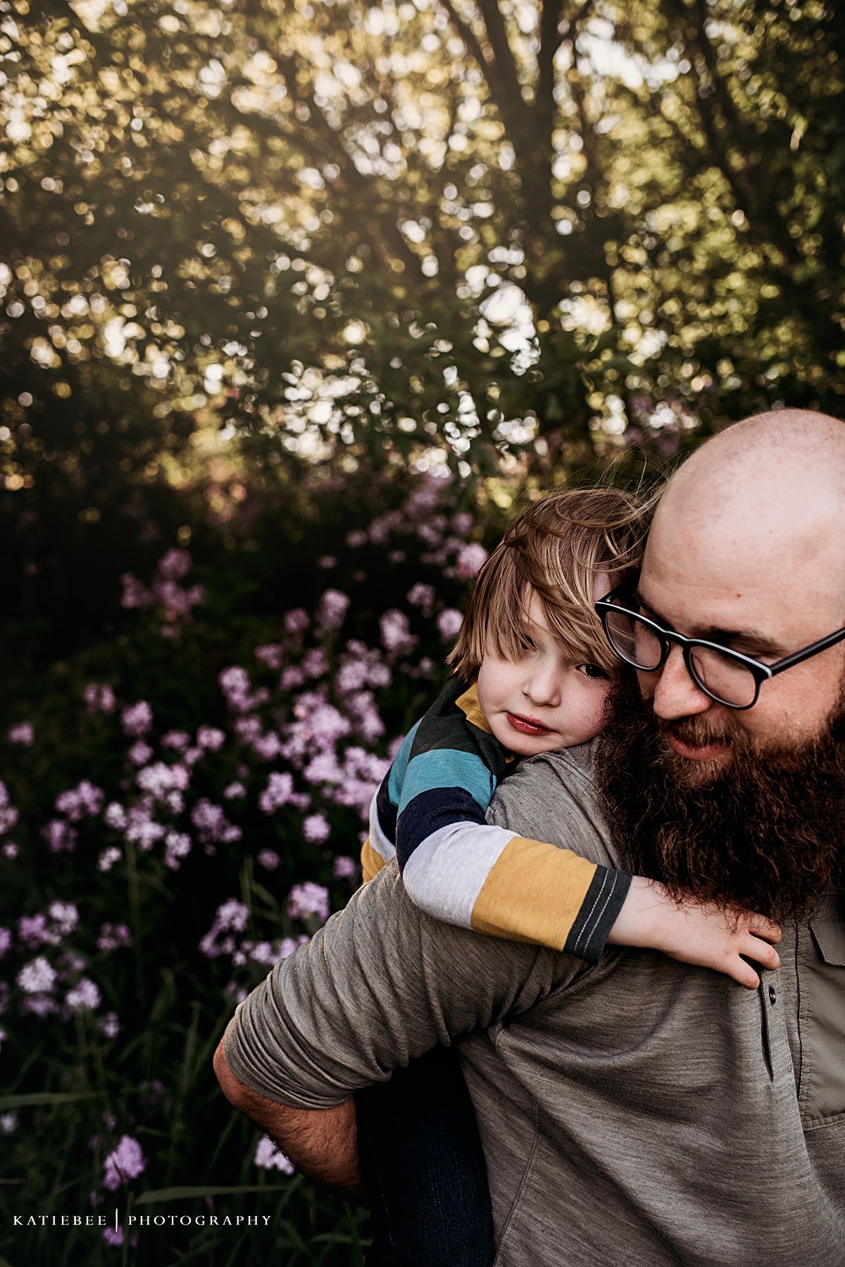 Intimate candid moment between parent and child against garden backdrop with purple flowers.